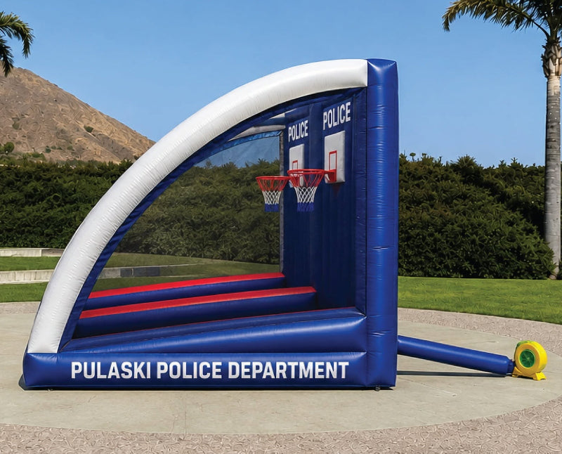 An inflatable outdoor bounce house with a basketball hoop, branded 'PULASKI POLICE DEPARTMENT', set up on a concrete pad in a grassy park with palm trees and a mountain in the background.